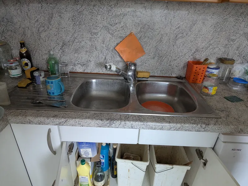 Spüle vorher: offener Unterschrank voller Putzmittel, Flaschen und Kleinkram rund um das Becken.